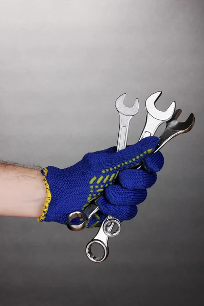 Wrenches in hand with protection glove on grey background