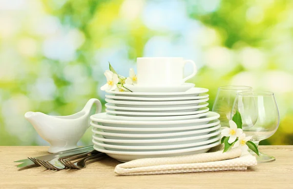 Empty clean plates, glasses and cup on wooden table on green background