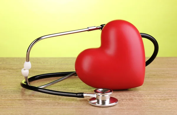 Medical stethoscope and heart on wooden table on green background