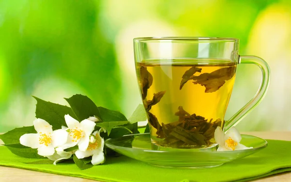Cup of green tea with jasmine flowers on wooden table on green background