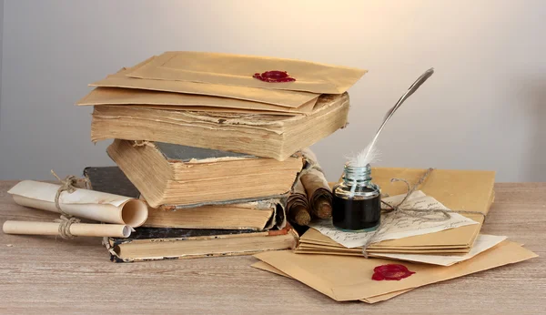 Old books, scrolls, feather pen and inkwell on wooden table on grey background