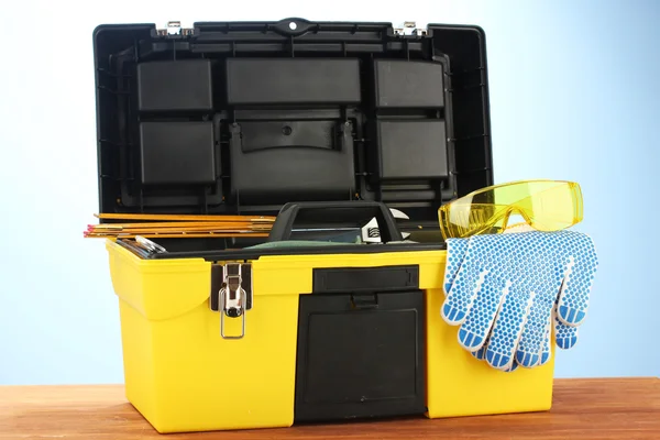 Open yellow tool box with tools on blue background close-up