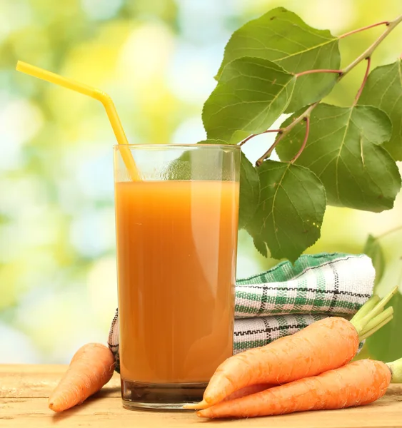 Glass of carrot juice and fresh carrots on wooden table on green background