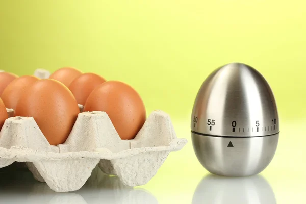 Eggs in box and egg timer on green background