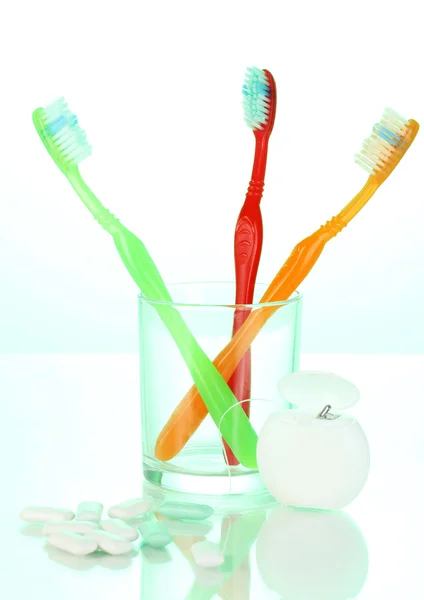 Toothbrush in glass, dental floss and chewing gum on green background