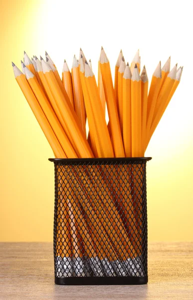 Lead pencils in metal cup on wooden table on yellow background