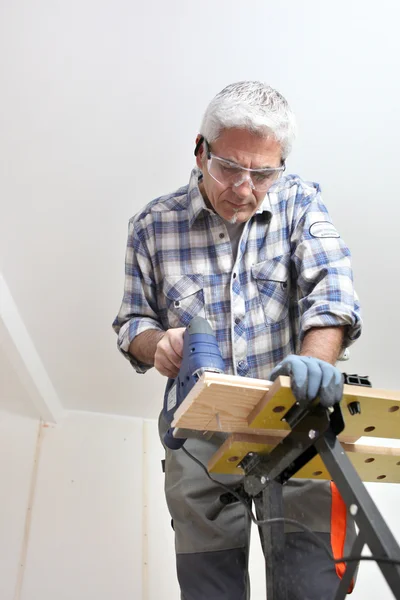 Grey-haired DIY fan drilling hole in wood