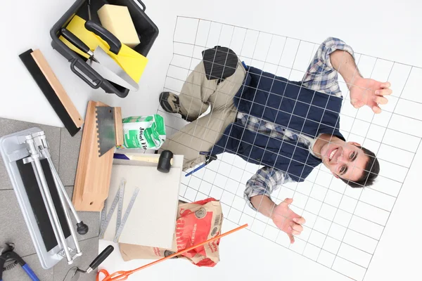 Tradesman posing with a metal grid, tools, and building materials