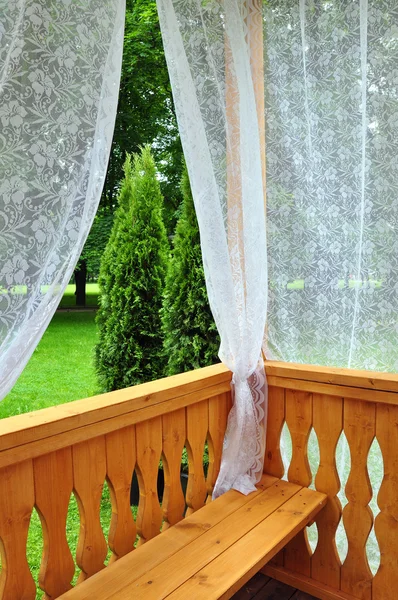 Wooden porch with lace curtains and garden view