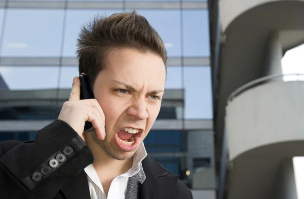 Young upset man shouting on mobile phone outdoors