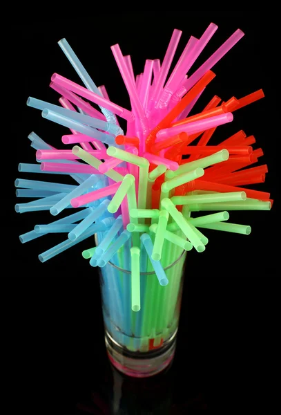 Long drink glass with some water and many colored plastic straws