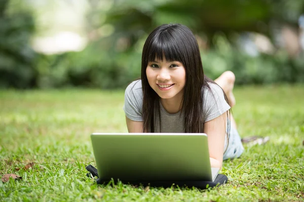 Chinese student lying in the park with her laptop