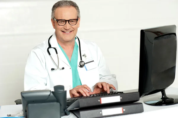 Aged male doctor in glasses working on computer