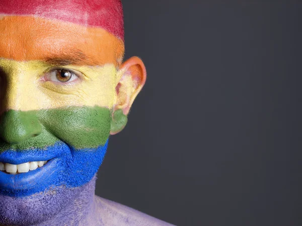 Gay flag painted on the face of a smiling man.