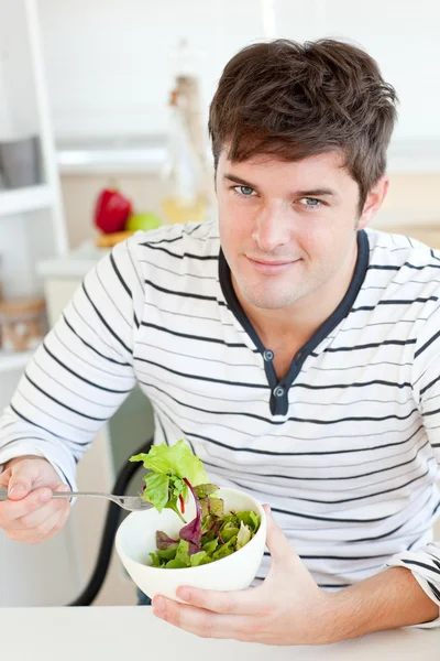 Handsome young man eating a healthy salad in the kitchen
