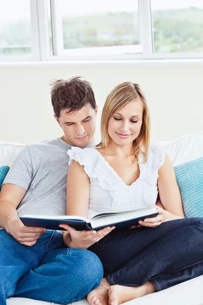 Smart couple reading a book together sitting on the sofa