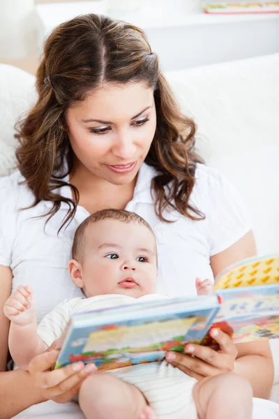 Attentive mother reading a book to her adorable baby sitting in