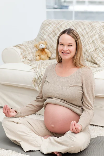 Pregnant woman doing yoga on the floor and smiling