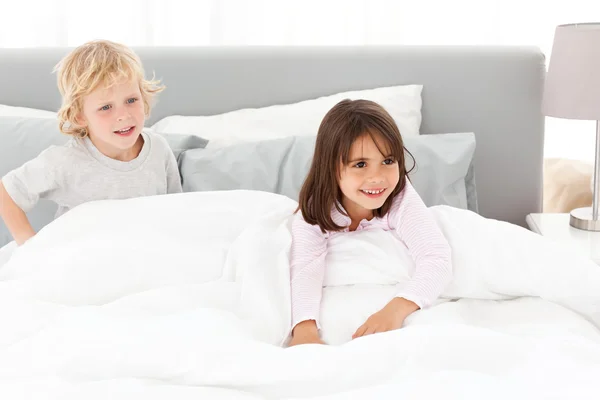 Happy brother and sister playing in their parents\' bedroom