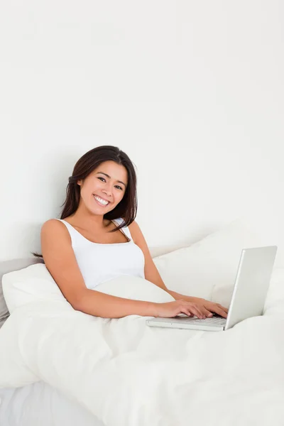 Smiling woman with notebook lying in bed looking into camera