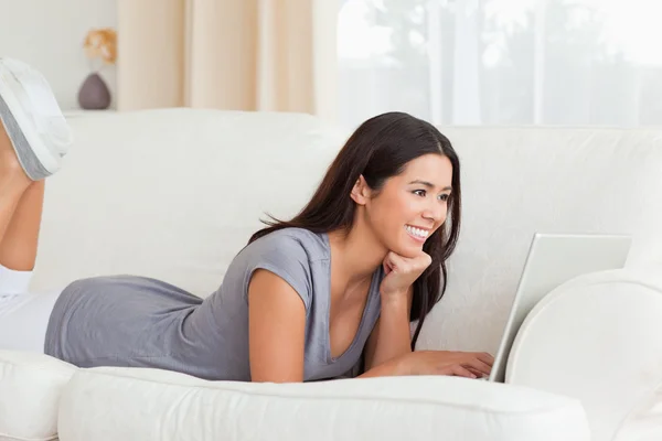 Happy woman lying on sofa with notebook in front of her