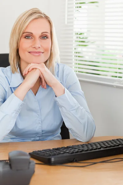 Charming blonde woman with chin on her hands behind a desk