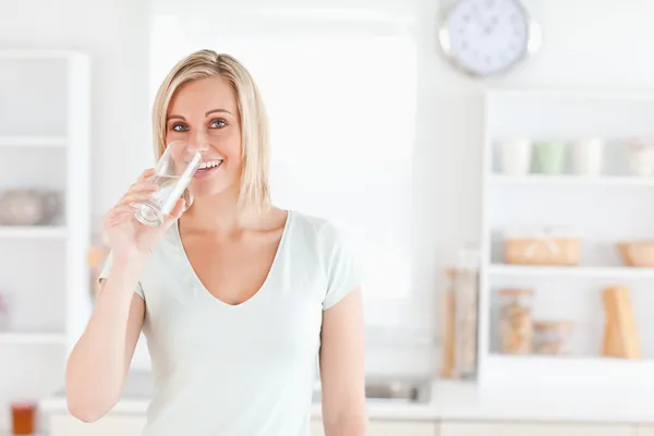 Charming woman drinking water while standing looks into camera