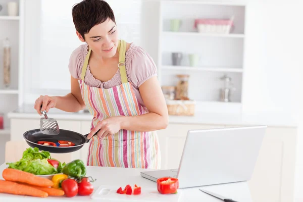 Beautiful woman cooking with receipt on laptop