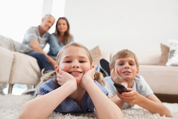 Siblings watching television with their parents on the backgroun