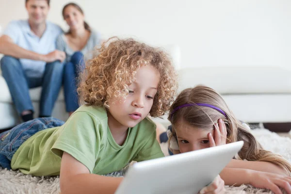 Young children using a tablet computer while their happy parents