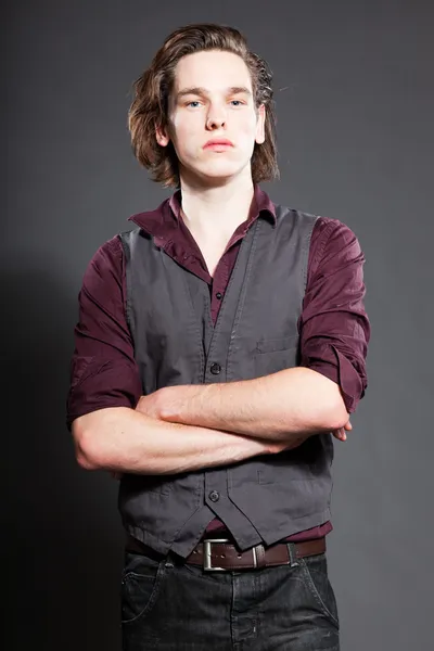 Handsome young man with brown long hair isolated on grey background. Fashion studio shot. Expressive face.