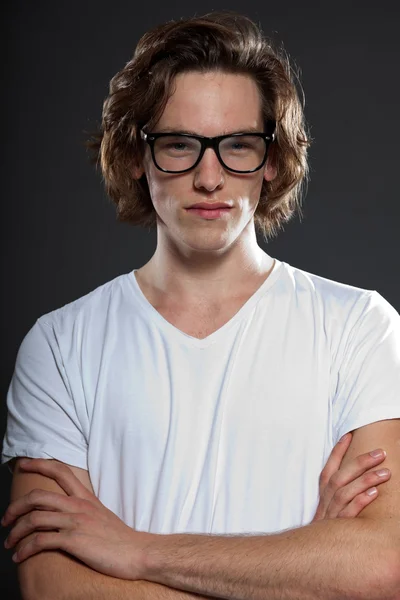 Handsome young man with brown long hair and retro glasses isolated on grey background. Fashion studio shot.