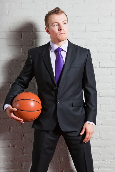 Business man with basketball. Good looking young man with short blond hair. Gym indoor.