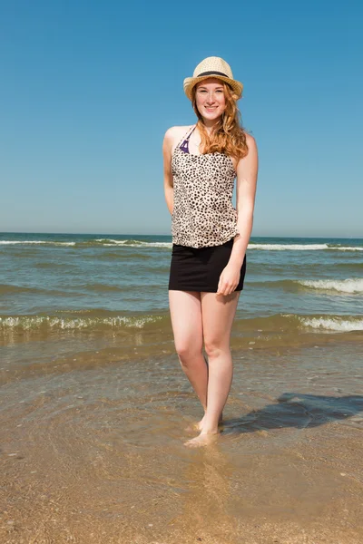 Happy pretty girl with long red hair and hat enjoying the refreshing beach on hot summers day. Clear blue sky.