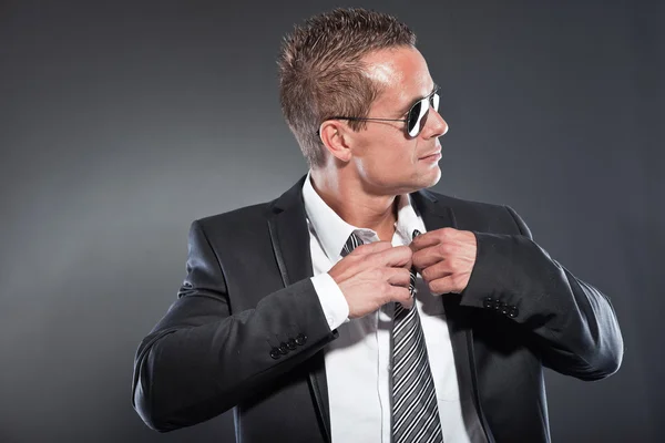 Good looking business man with black sunglasses and short blond hair. Tough guy. Wearing tie and black jacket.