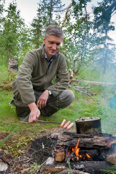 A man cooks sausages on the fire