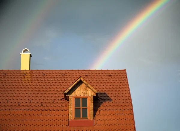 Rainbow beyond a reddish roof of a house
