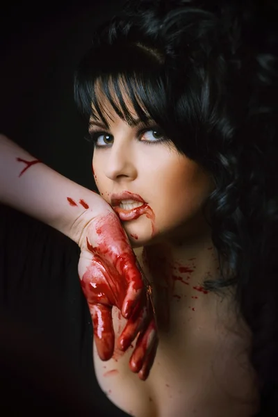 Beauty vampire girl with blood on face on black background