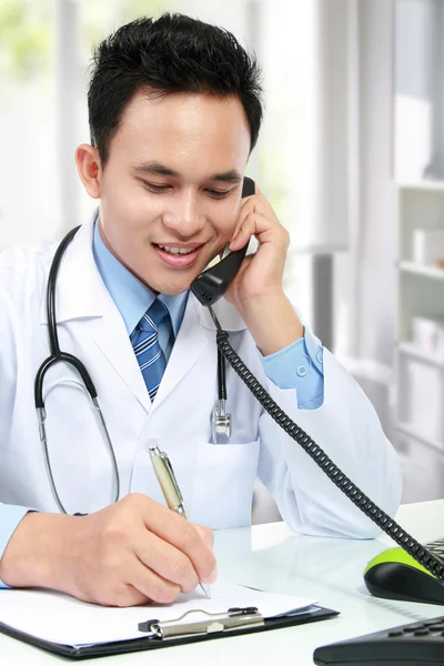Medical doctor writing a note while calling