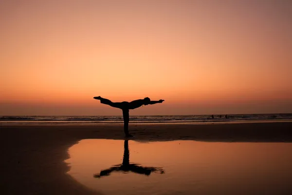 A man silhouette in a yoga warrior pose on a sunset seashore background