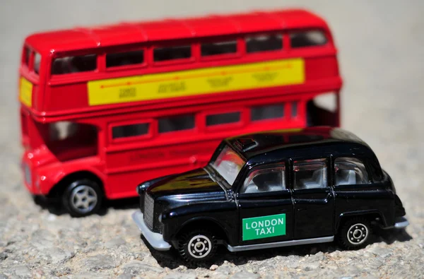 A bright red traditional London Bus and Black Taxi isolated over tar-seal.