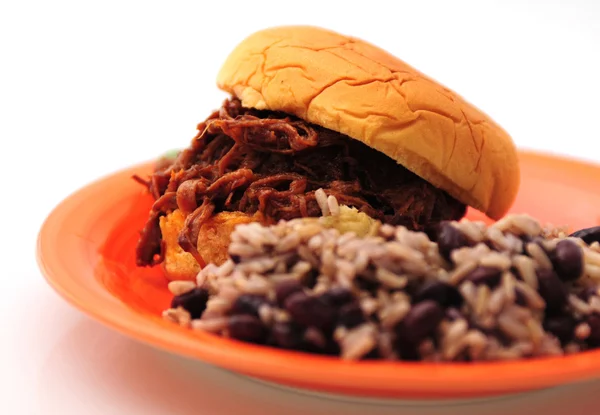 Shredded beef sandwich on an orange plate with beans and rice