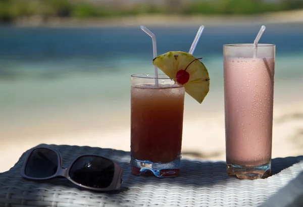 Beverages and sunglasses on a bedside cabinet on a beach.