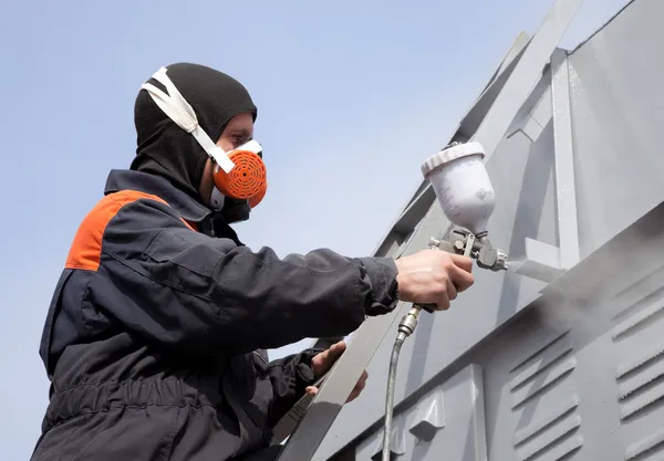 A commercial painter on the stairs spray painting a steel exteri