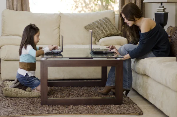 Young mother and daughter using their laptops in the living room