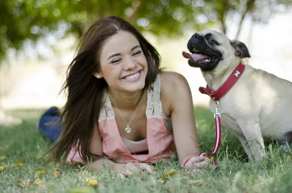 Cute young woman spending some time with her pug dog at the park
