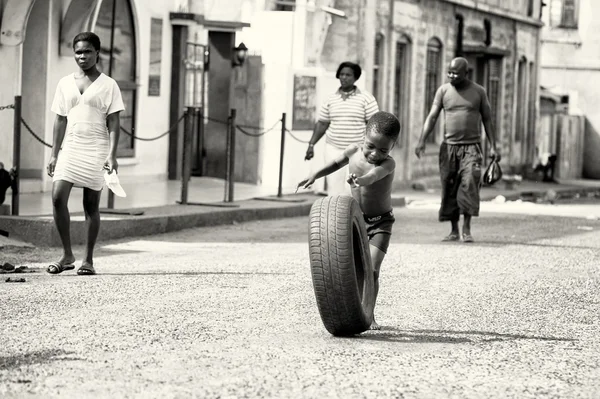 Little Ghanaian boy runs across the street with a tire
