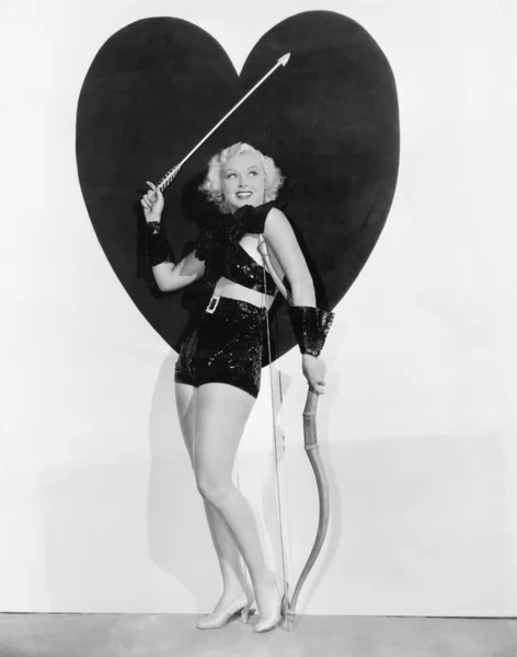 Young woman dressed up as cupid standing in front of a big heart