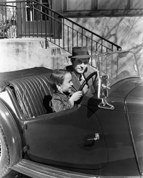 Young boy sitting in the driver\'s seat of car with his father
