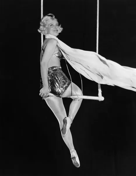 Profile of a female circus performer performing on a trapeze bar